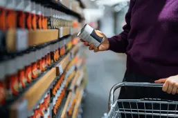 Cropped shot of young woman pushing a shopping cart, grocery shopping in supermarket. She is holding a tin can and reading the nutritional label.
