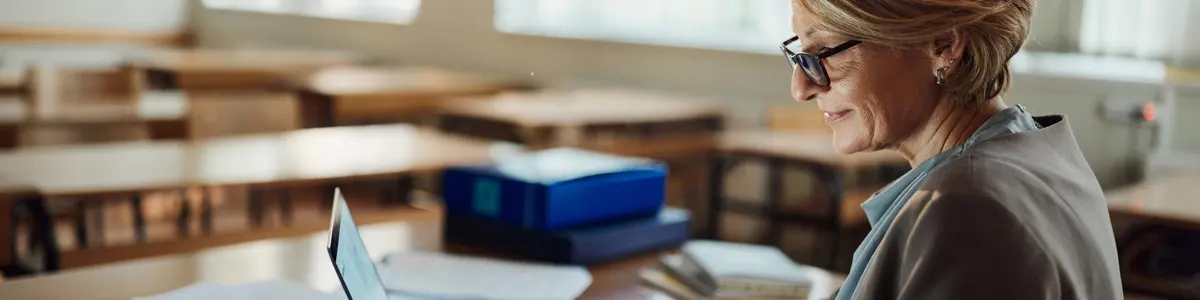 Maestra sonriente trabajando en su computadora portátil en el salón de clases