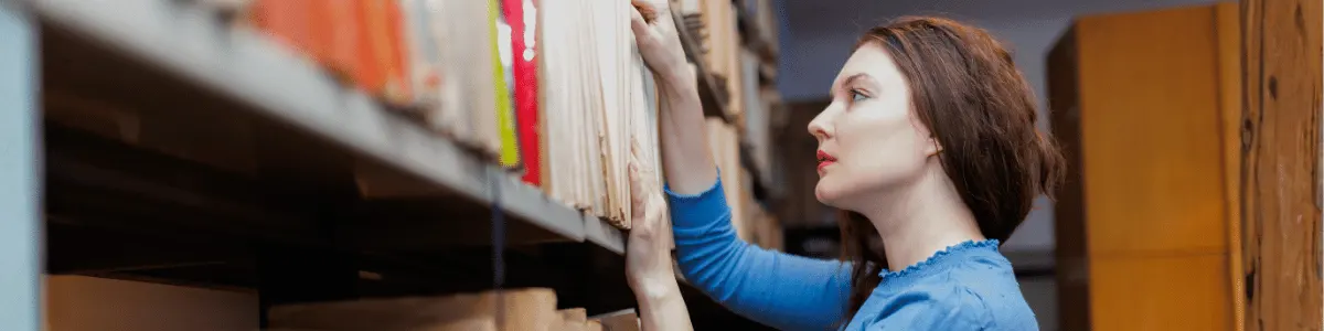 Female post-grad searching for study material, standing by the library shelves