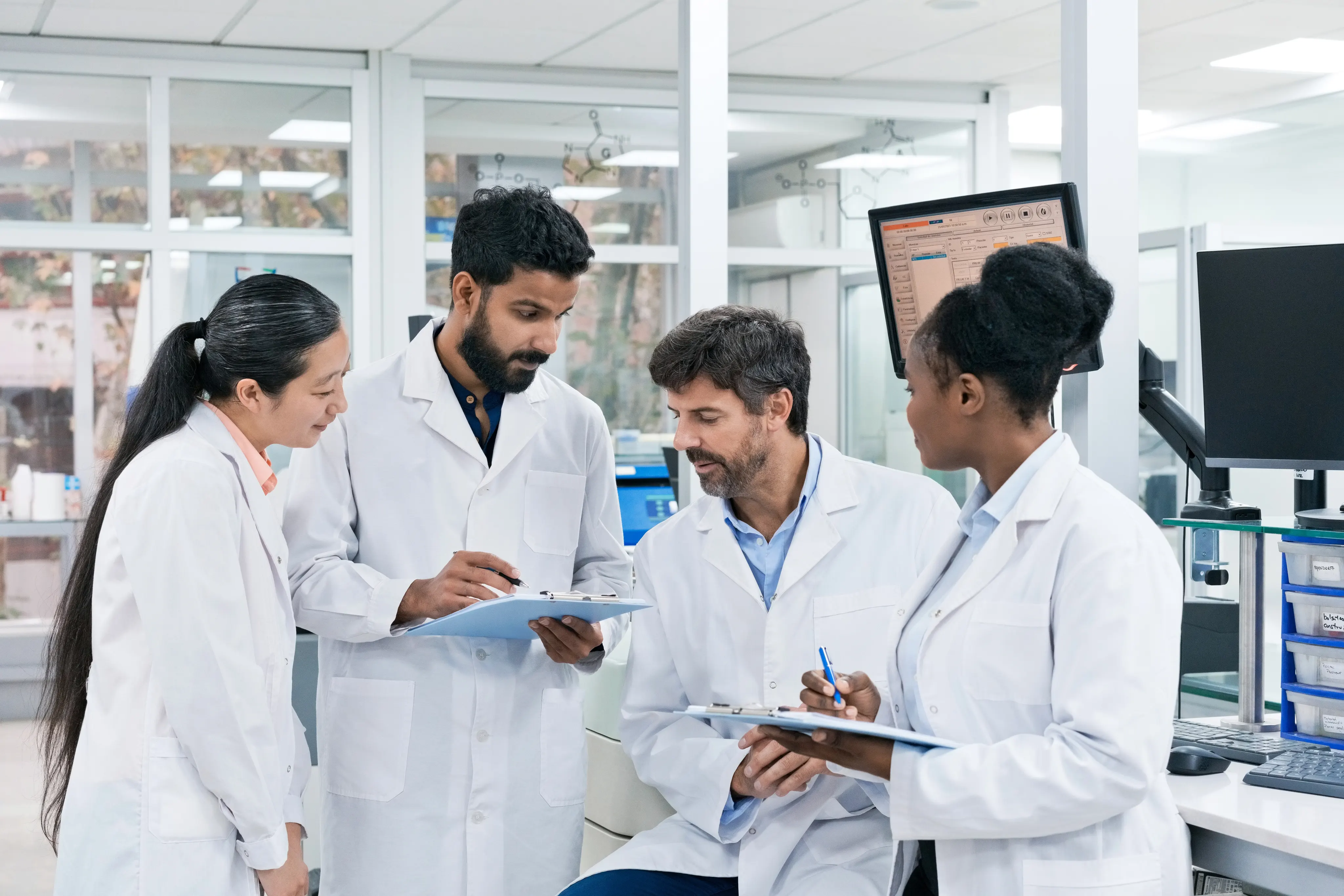 Team of biochemists discussing over while writing on clipboards at laboratory