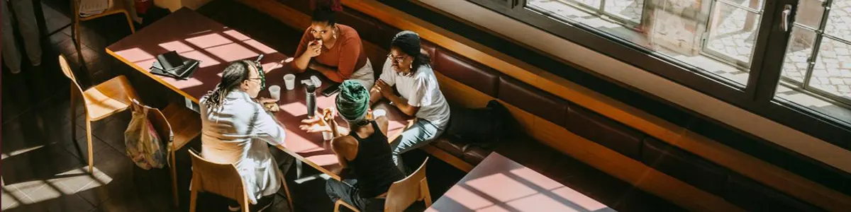 Teacher with female students discussing while sitting in college cafeteria