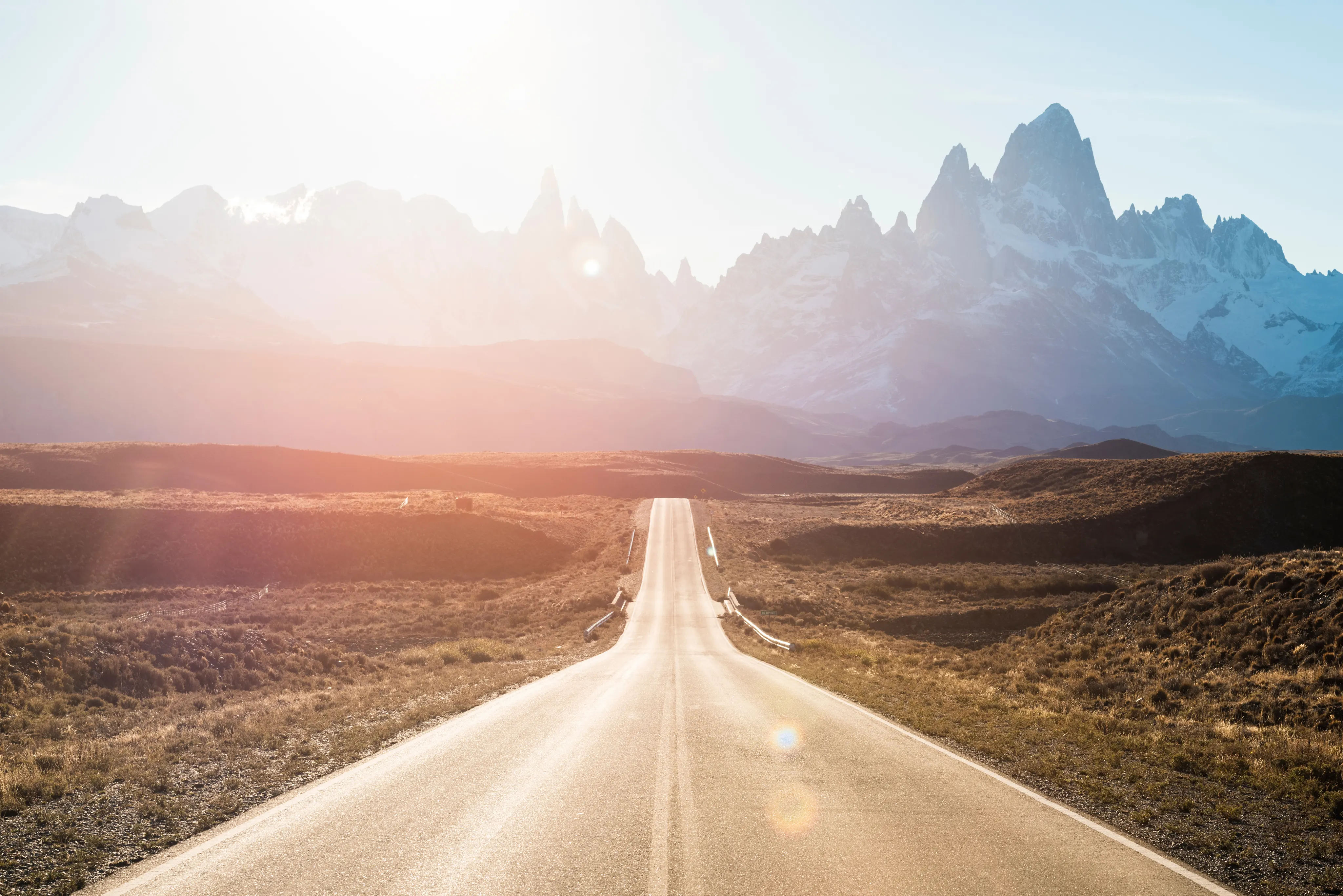 image of a road heading towards mountains with the sun shining