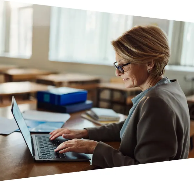 Smiling female teacher working on laptop in the classroom
