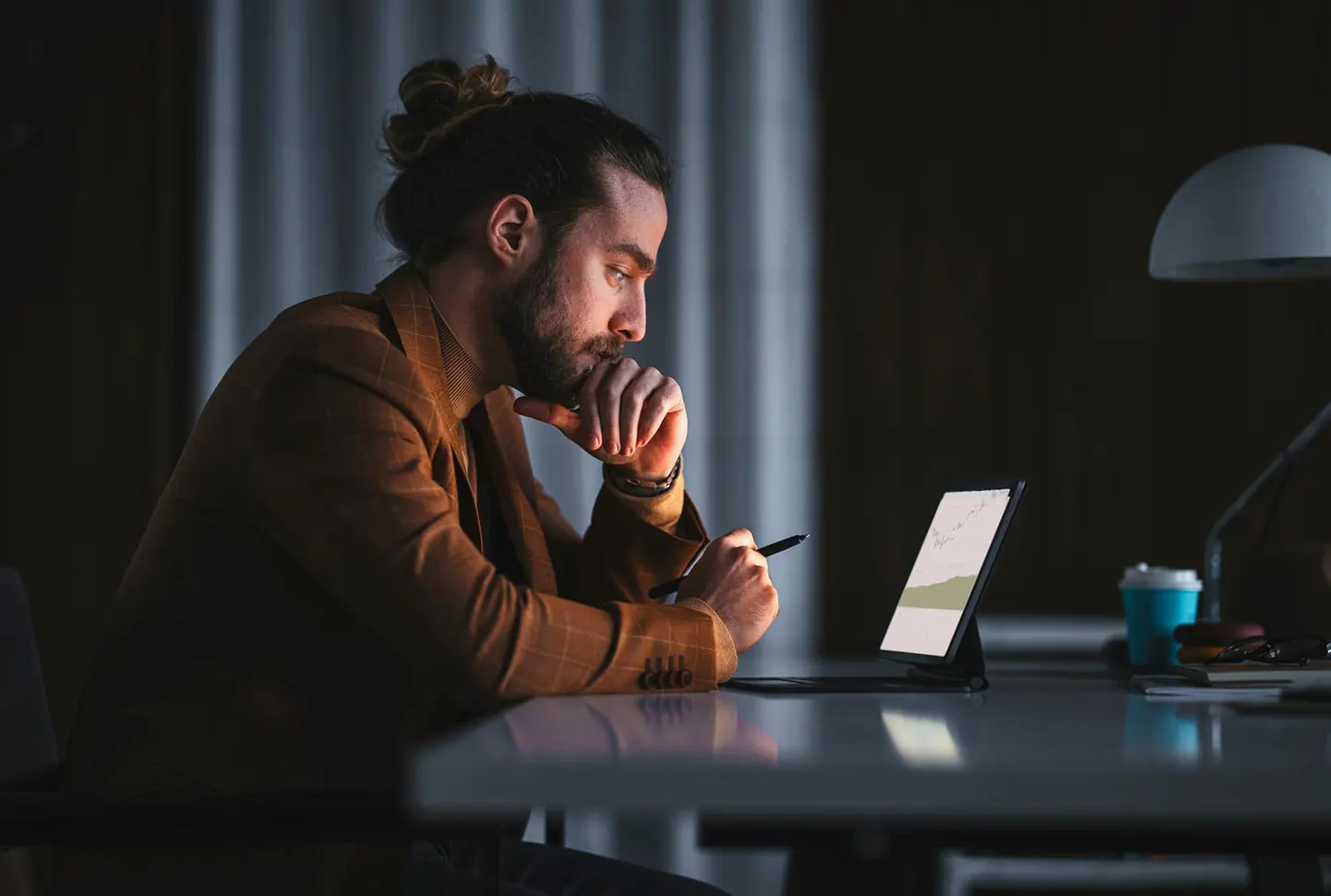 Side view of thoughtful adult male sitting at table with laptop