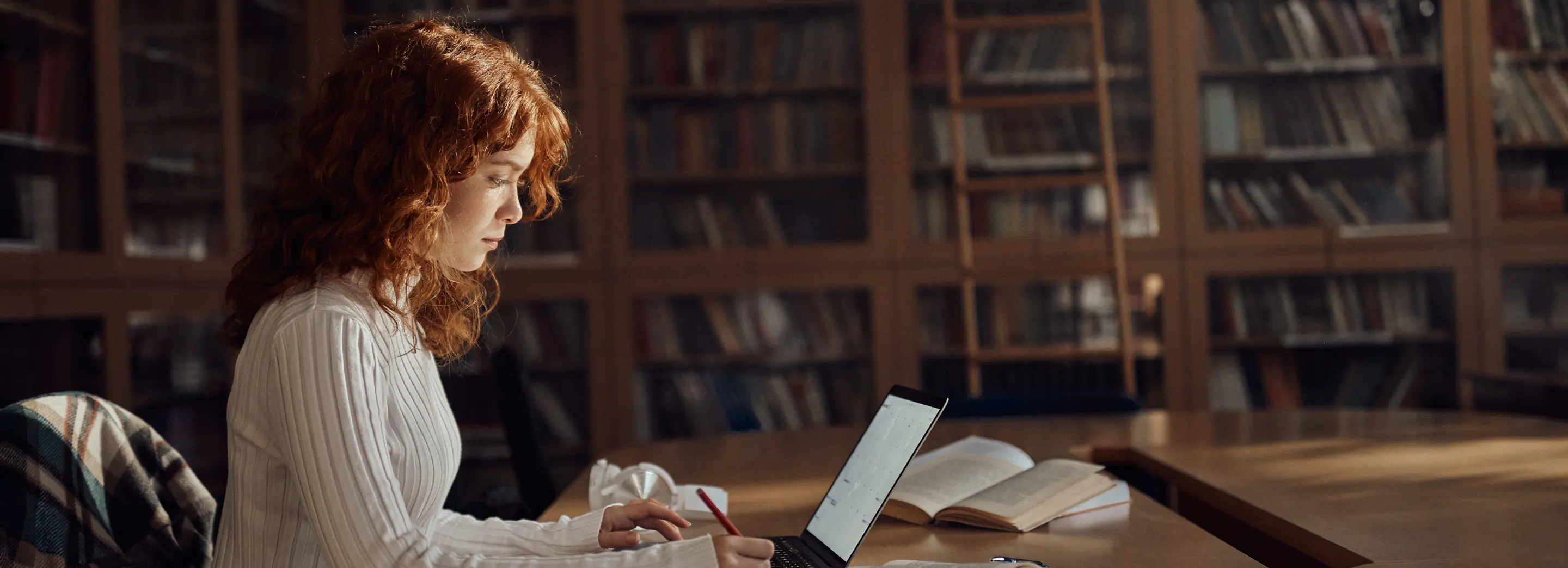 A woman looking in front of her laptop inside a library