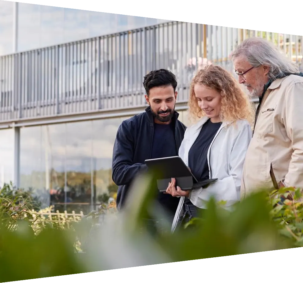 Two men and a woman standing looking at laptop in courtyard