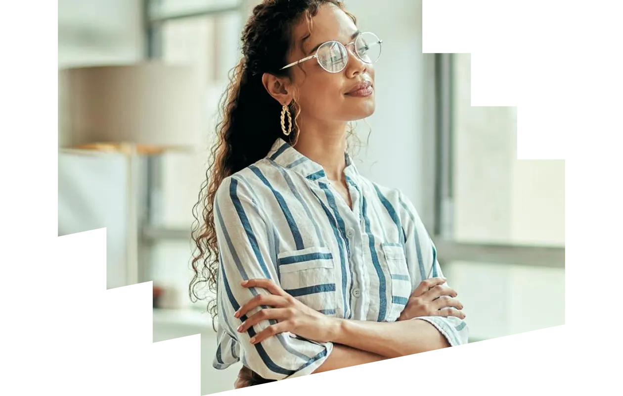 Thoughtful female entrepreneur wearing glasses standing next to window with her arms crossed