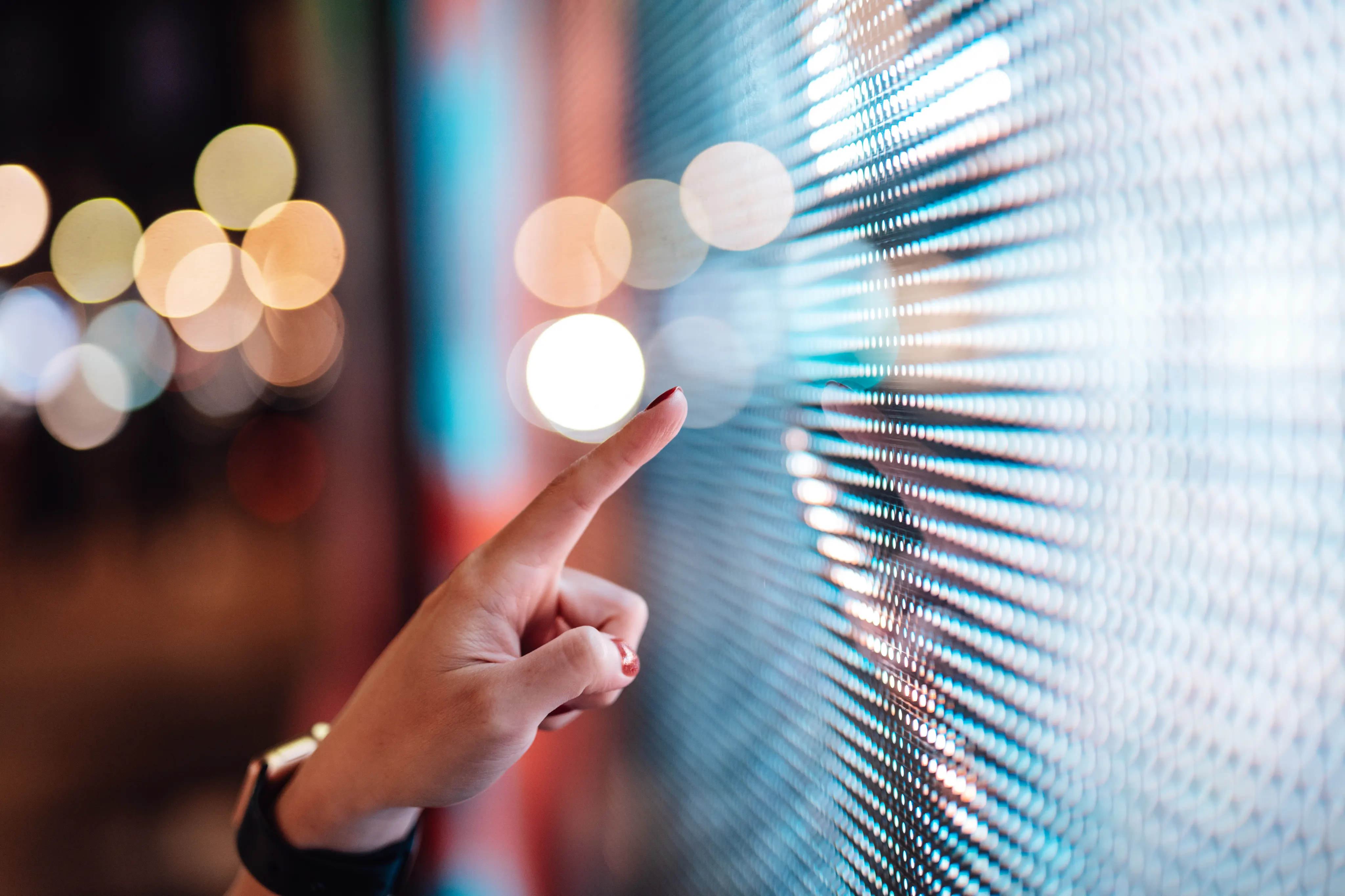 Close-up of female finger touching futuristic LED display board in the city