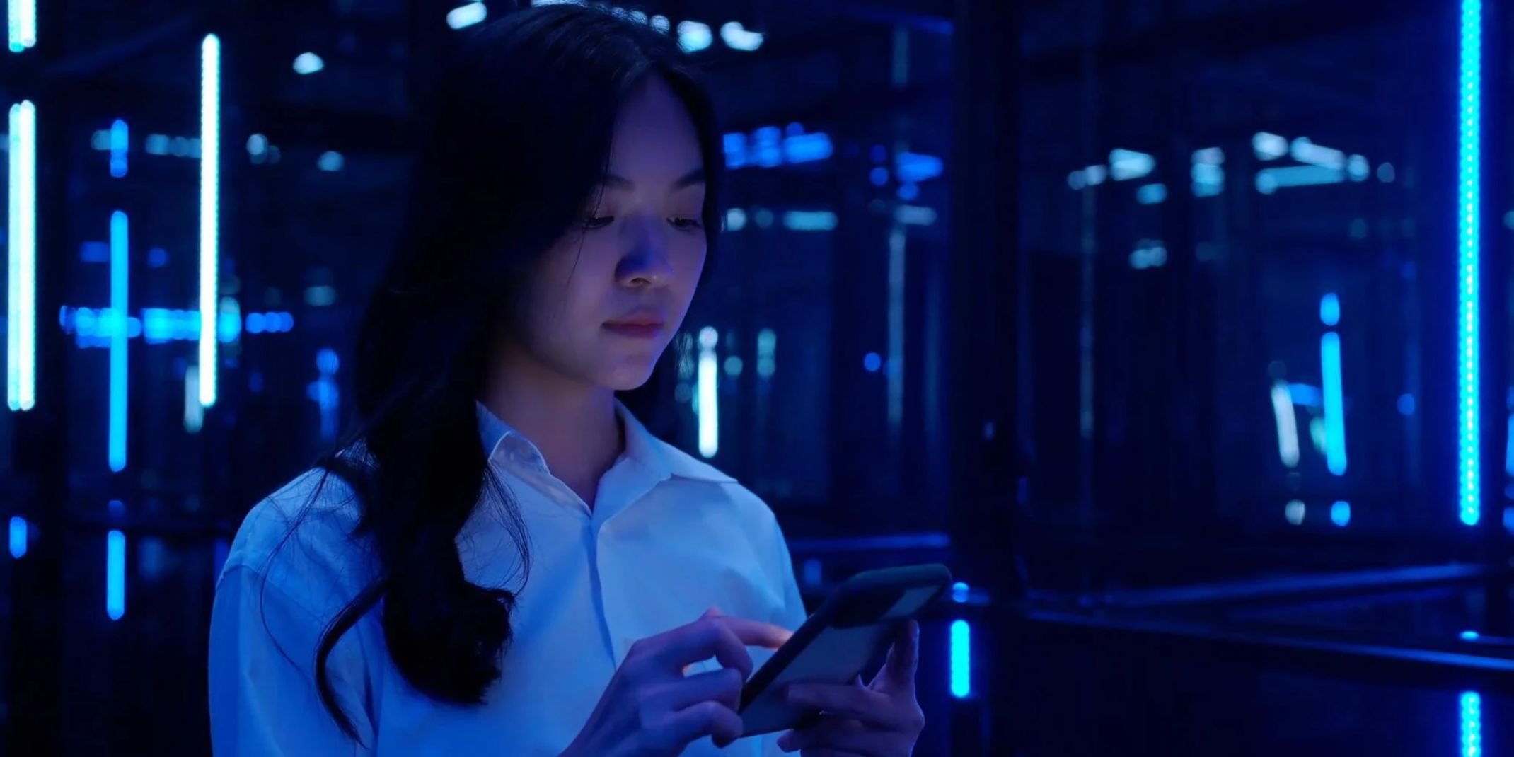 Asian teenage girl using mobile smart phone with a 5G while looking in colourful UV lighting at dark night.
