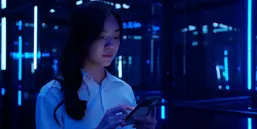 Asian teenage girl using mobile smart phone with a 5G while looking in colourful UV lighting at dark night.