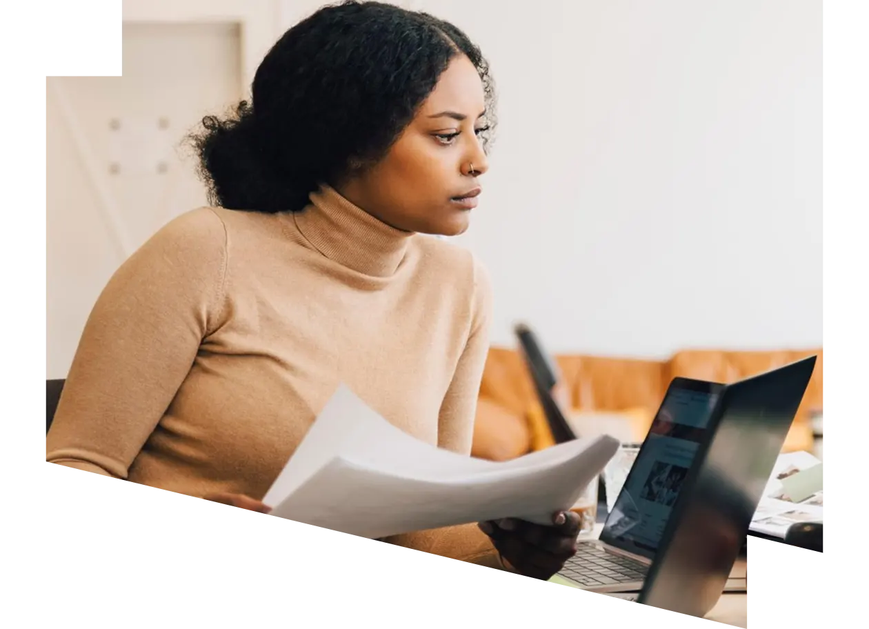 Focused female IT professional holding document while looking at computer