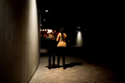 Two young women walking away in a dimly lit urban underpass at night, shadows stretching around them, evoking feelings of mystery and solitude
