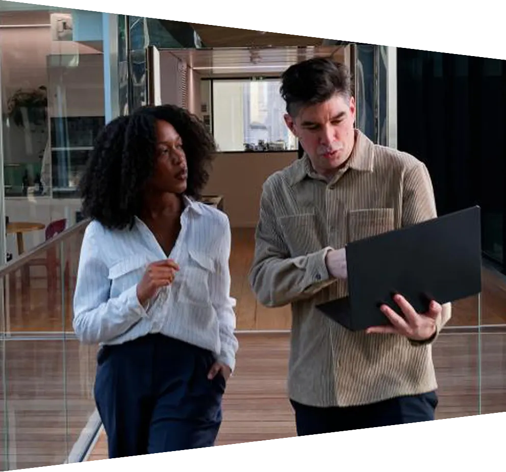 Colleagues walking across elevated bridge in modern office and looking at laptop