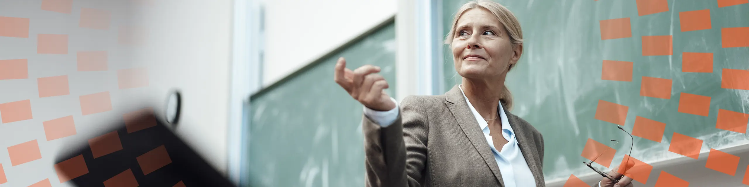 A woman speaking in front of her class with blackboard in the background