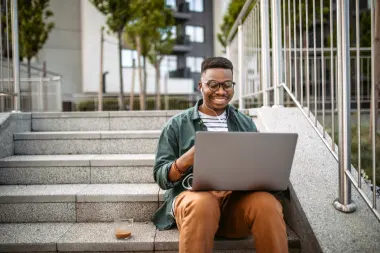 man working on laptop while sitting on stairs outside