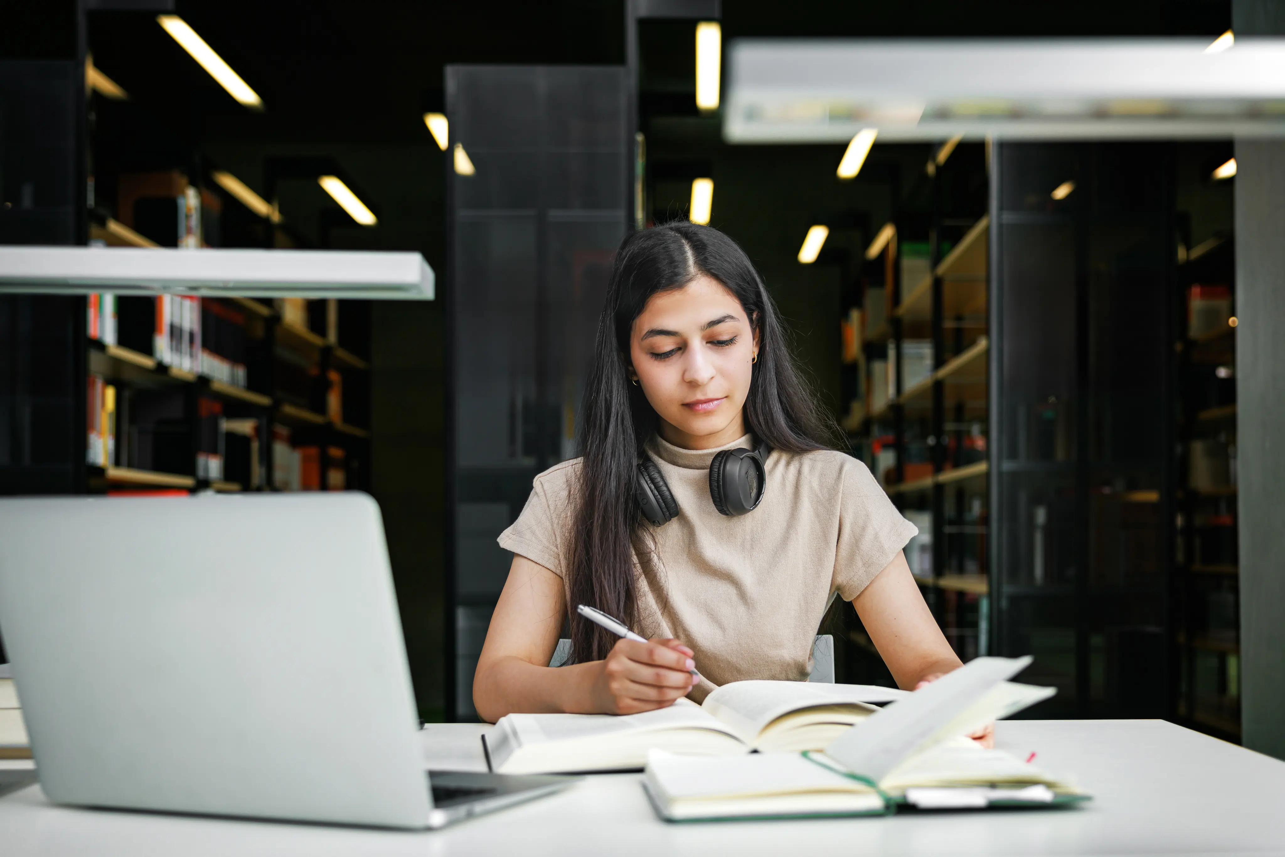 woman in library studying with book and laptop