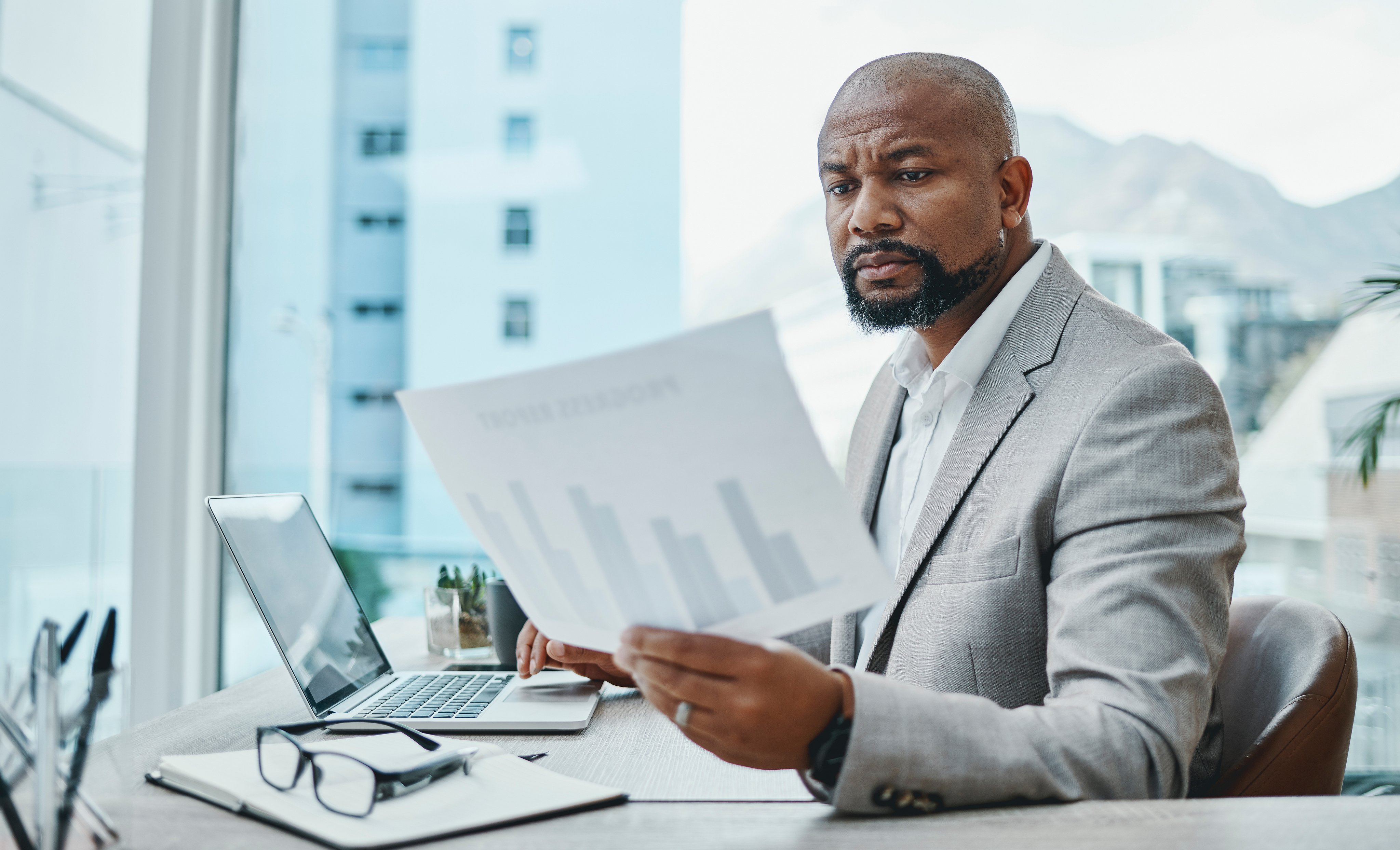 Shot of a mature businessman using a laptop and going over paperwork in a modern office