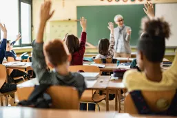 Rear-view-of-elementary-students-raising-hands-on-a-class