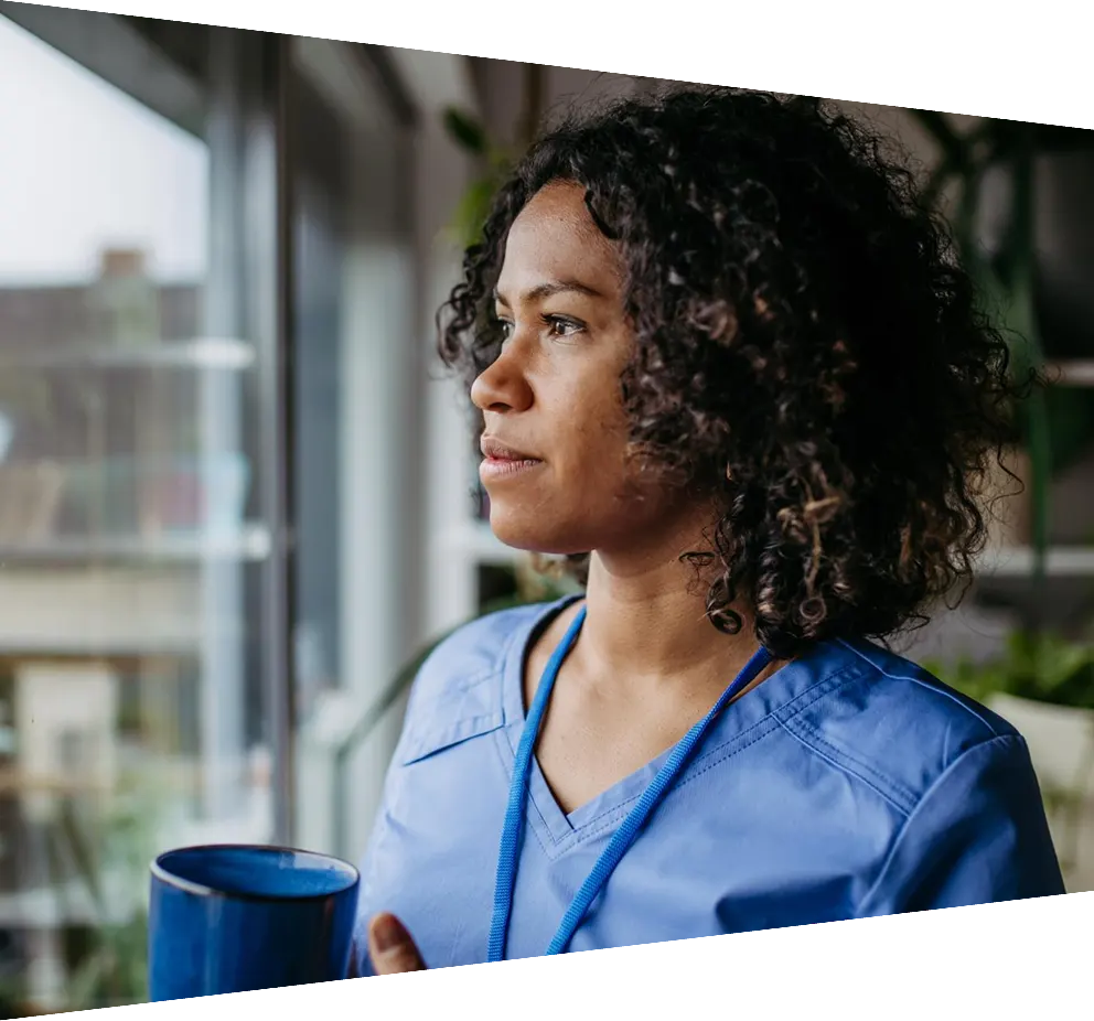 Female nurse enjoying cup of coffee standing by window in scrubs