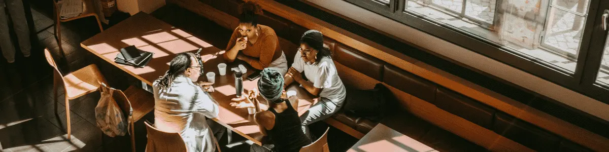 Teacher with female students discussing while sitting in college cafeteria