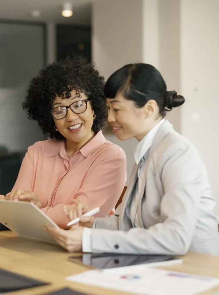 Businesswomen collaborating in office meeting using laptop and documents - mobile