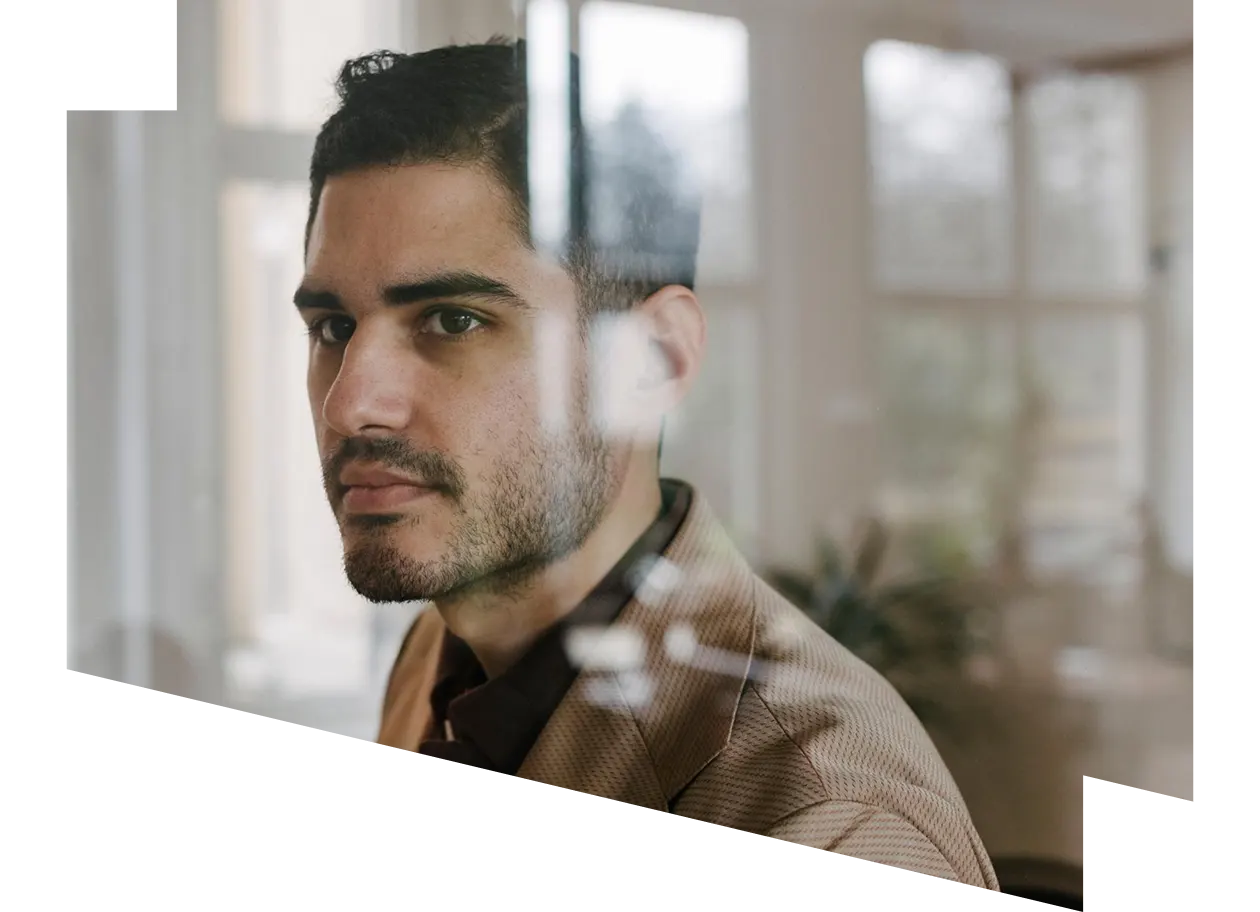 A contemplative businessman standing in his office behind a glass window pane