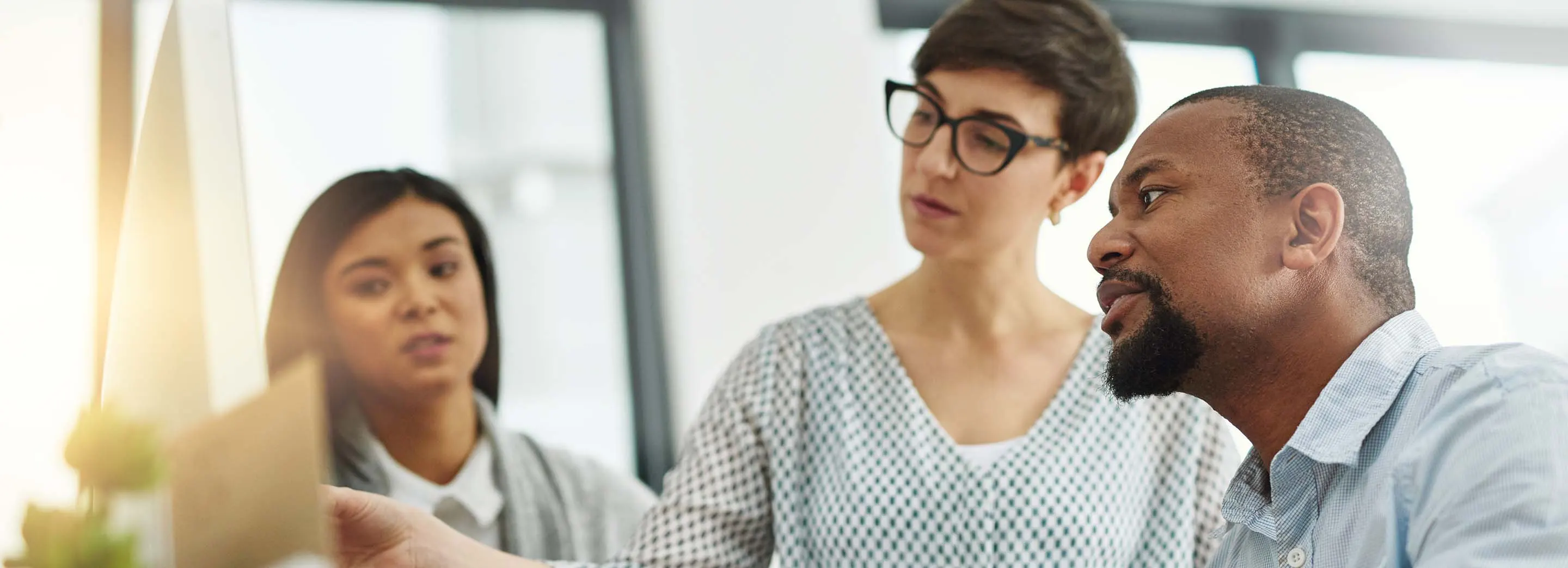 Team of professionals collaborating in an office meeting while reviewing documents on a computer screen