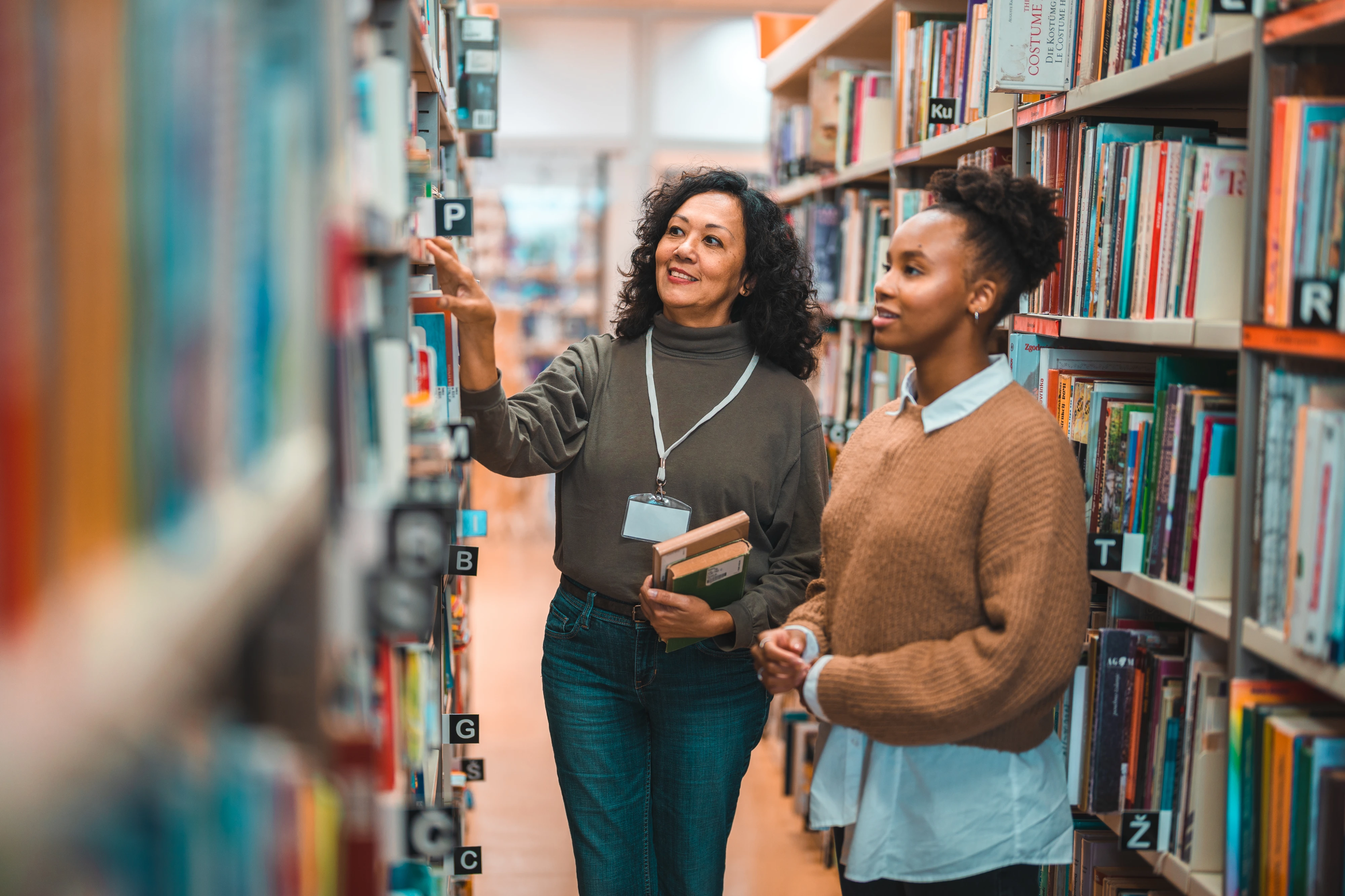 Mid Adult Hispanic Librarian Escorting A Student In A Library