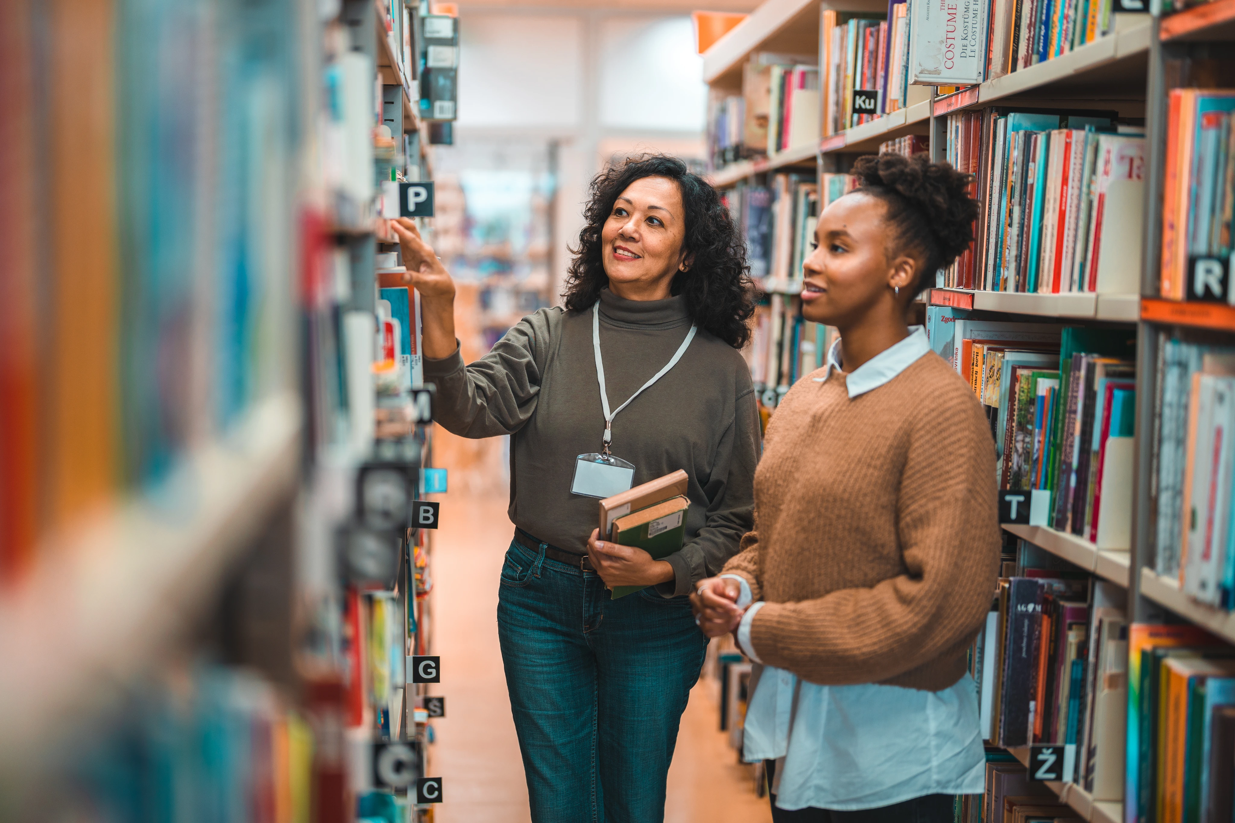 Mid Adult Hispanic Librarian Escorting A Student In A Library
