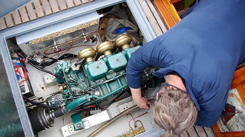 Bilde av båtmotor tatt ovenfra, med en mann som strekker seg ned og fikler med noe i motorrommet