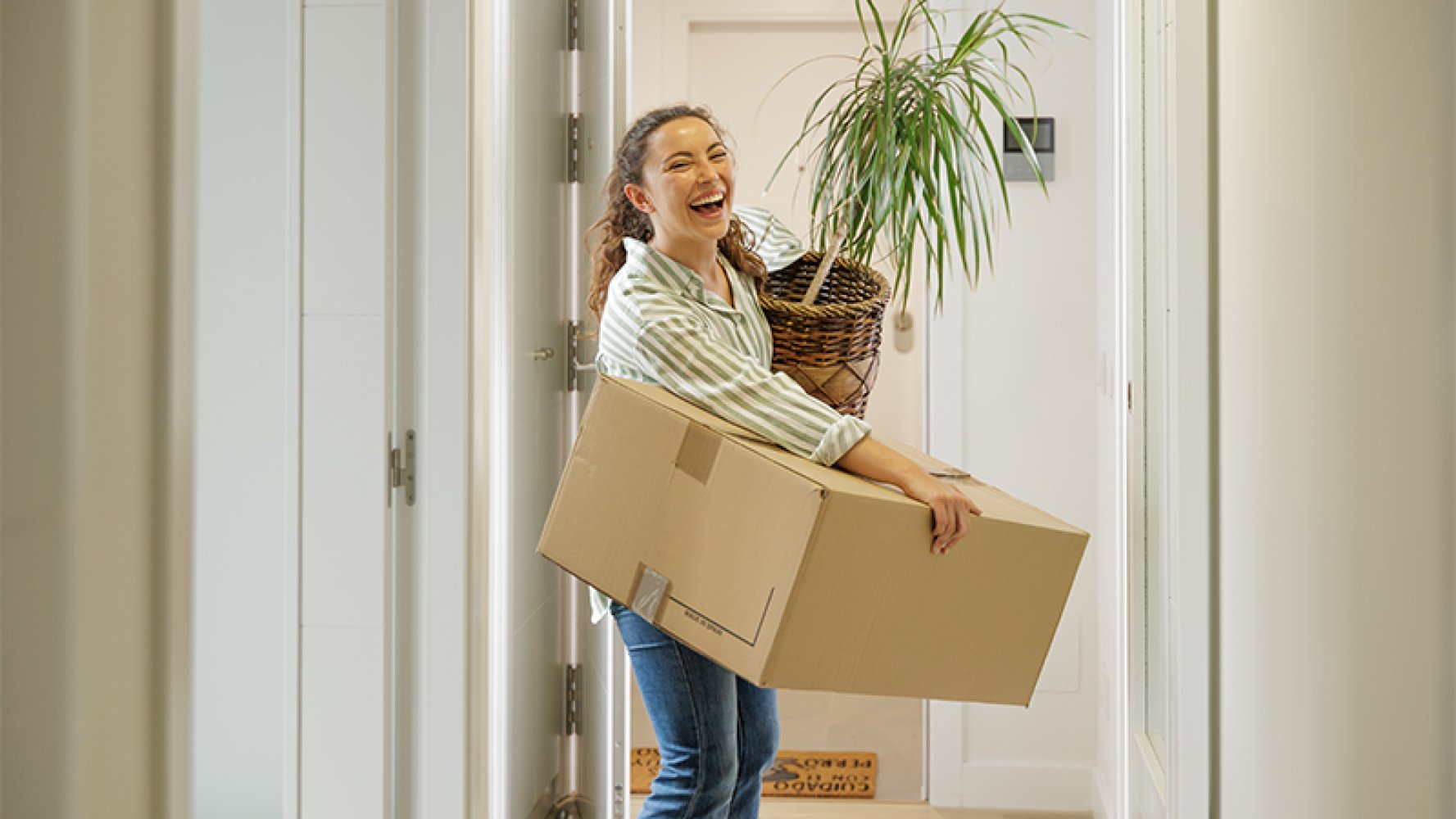 Dame kommer inn i en leilighet mens hun bærer en grønn plante og en pappeske