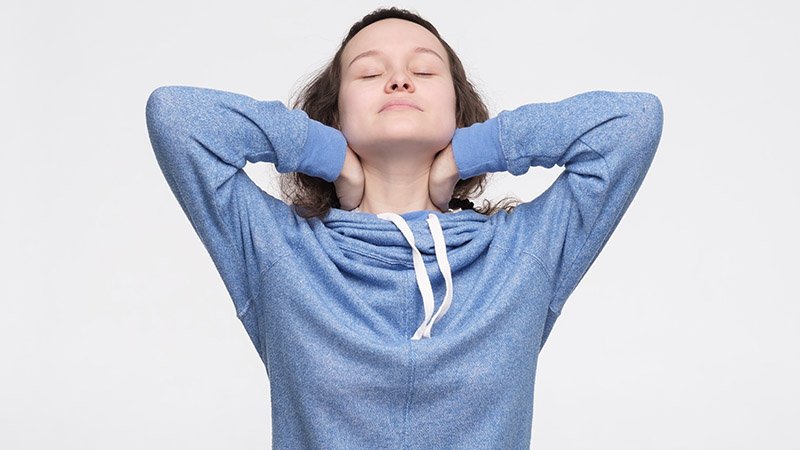 En ung kvinne holder på nakken sin med begge hender