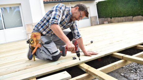 En mann skrur fast planker på en terrasse.