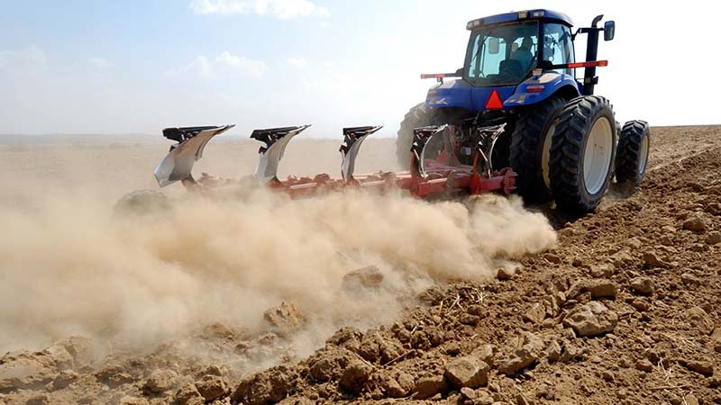 En traktor med traktorfres kjører over et tørt jorde.