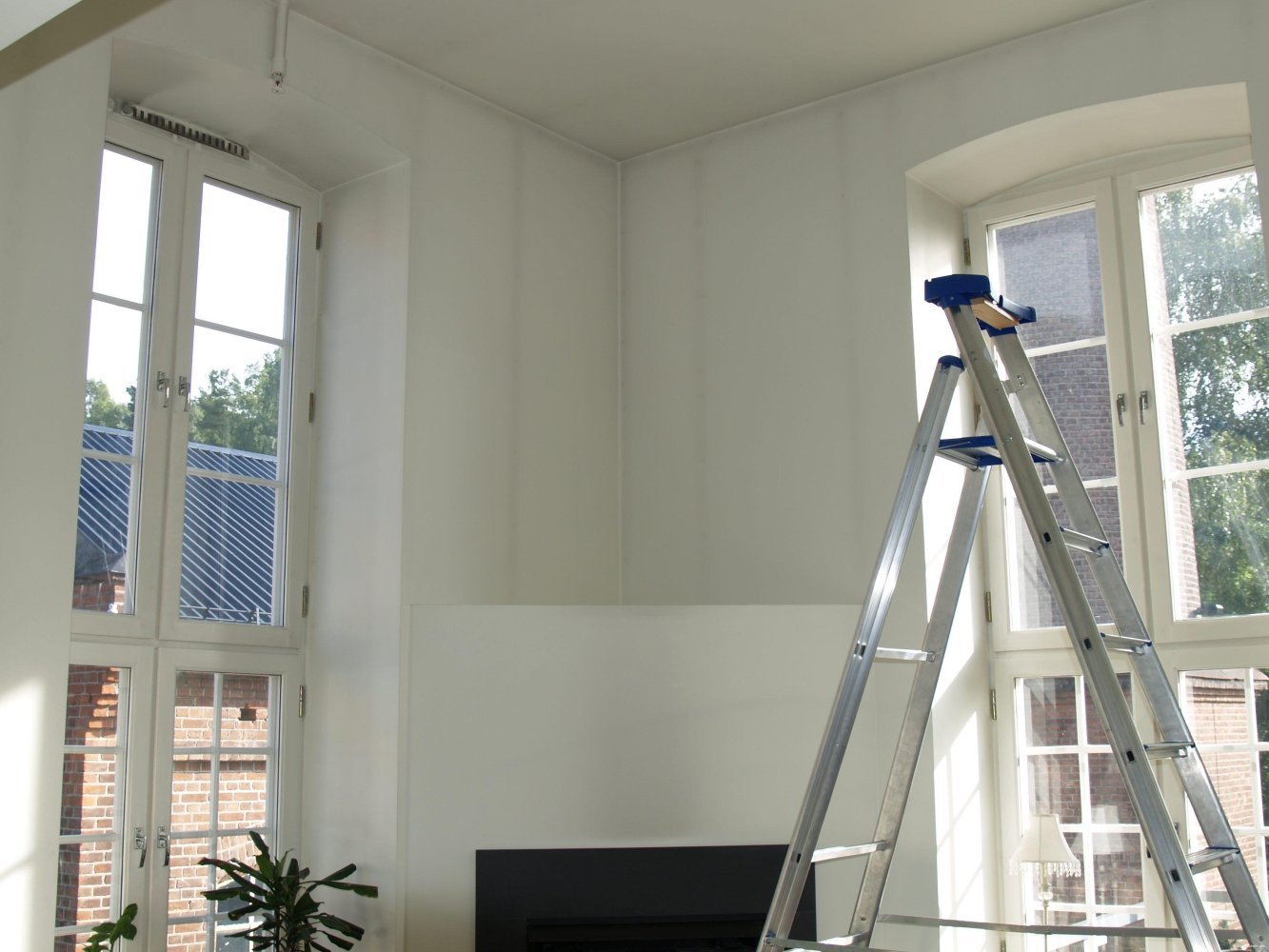 Stue under oppussing med store vinduer og en stige plassert mot veggen. Heksesot er synlig langs veggene.