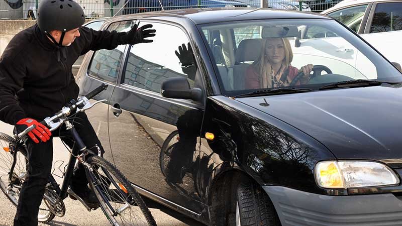 Syklist strekker ut armen mot en bil og ser frustrert ut.