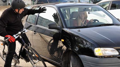 Syklist strekker ut armen mot en bil og ser frustrert ut.