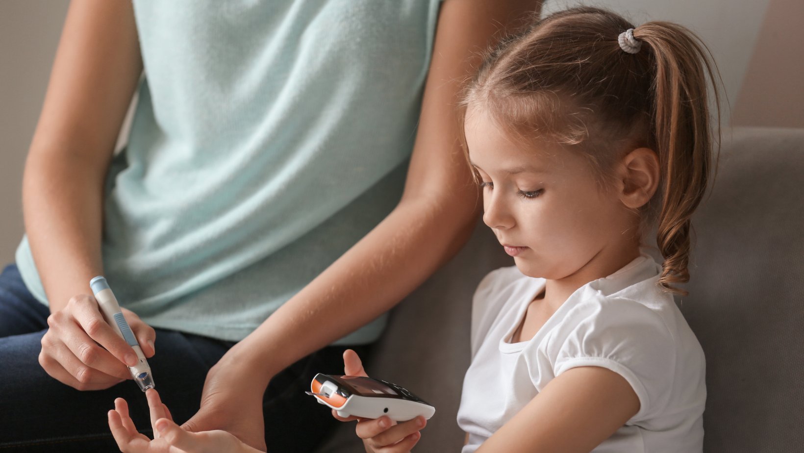 En jente med musefletter får hjelp av mammaen sin til å bruke blodsukkermåler.