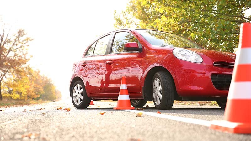 Bil står på vei mellom trafikkjegler omgitt av høsttrær.