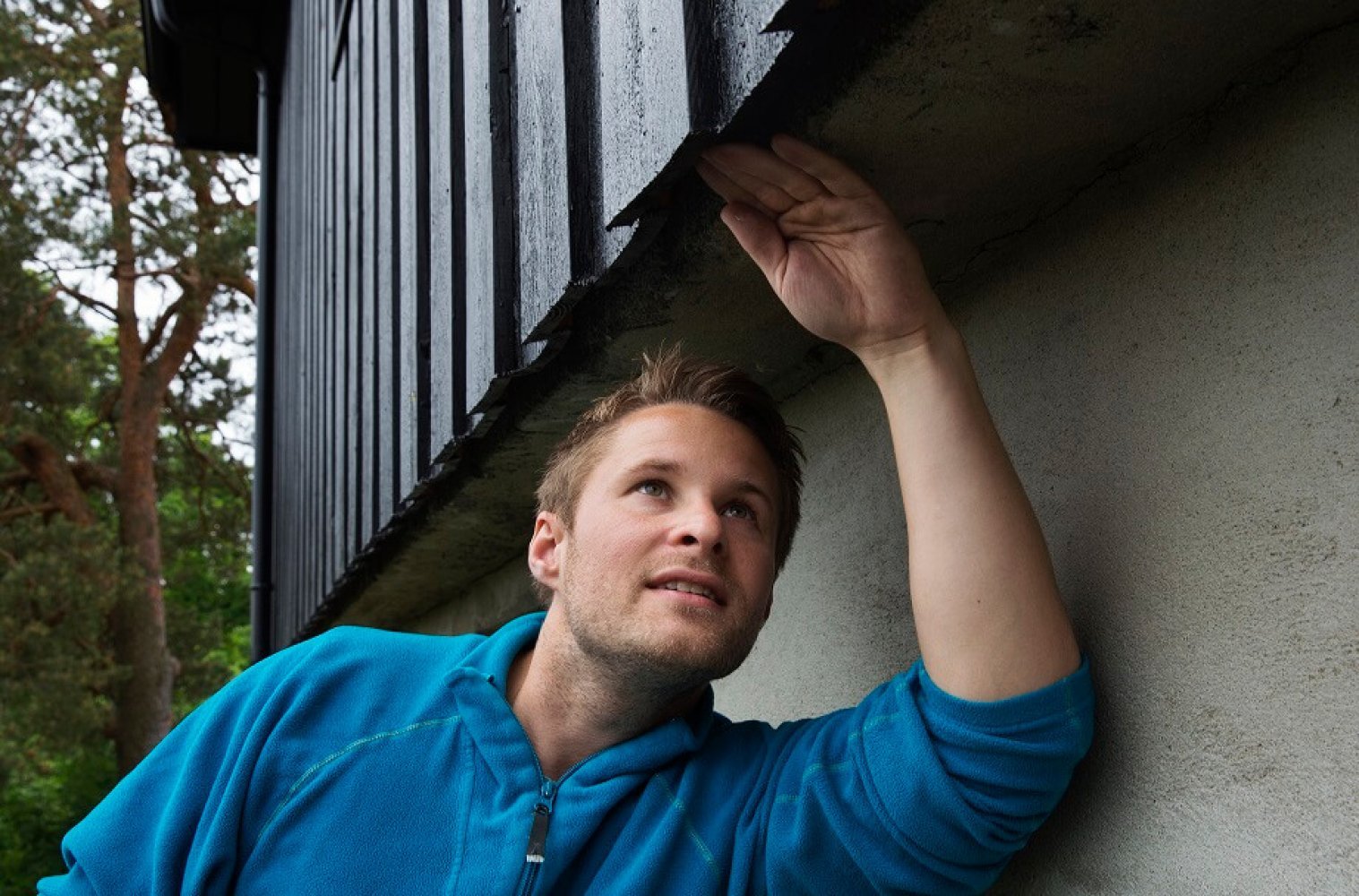 En mann inspiserer kledningen på et hus.