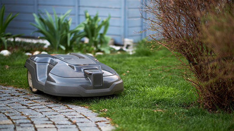 En robotgressklipper jobber i kanten av en brosteinsbelagt vei.