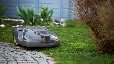 En robotgressklipper jobber i kanten av en brosteinsbelagt vei.