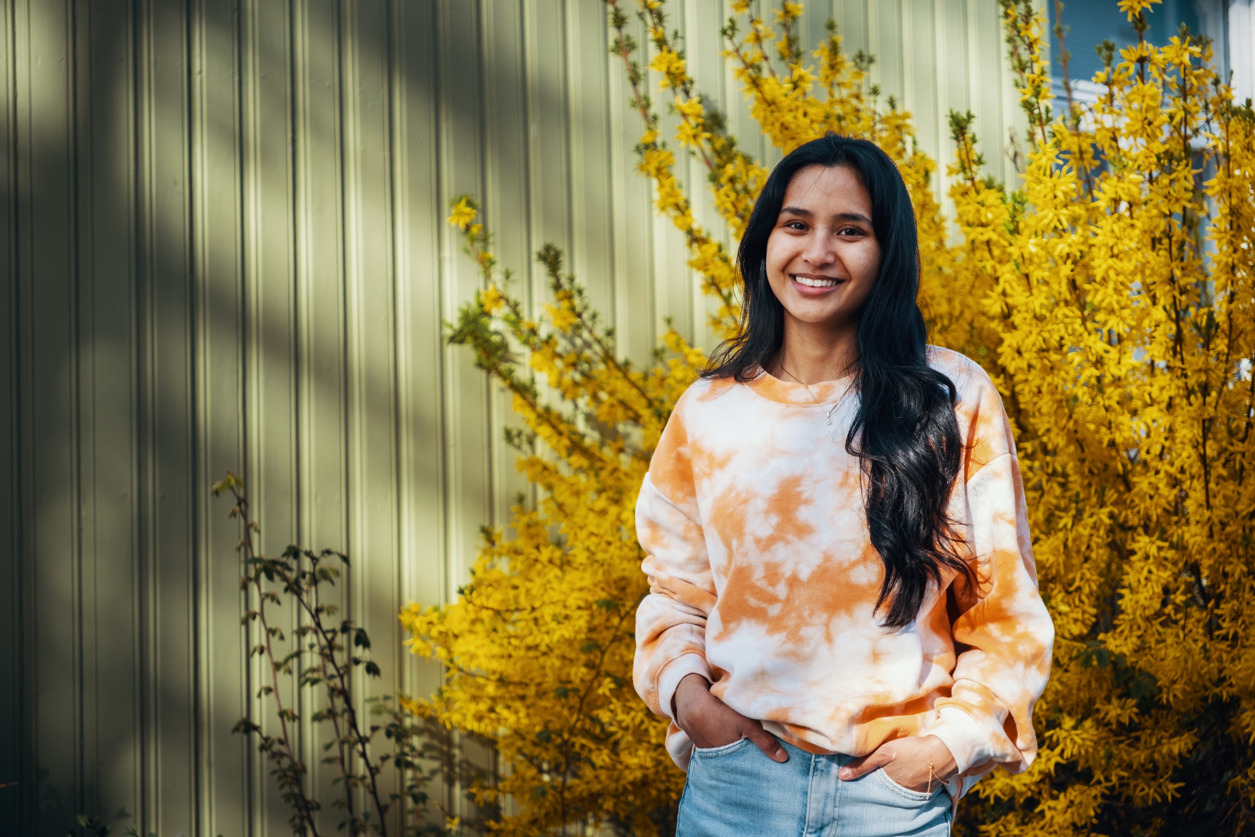 Ung kvinne står foran et hus og smiler.