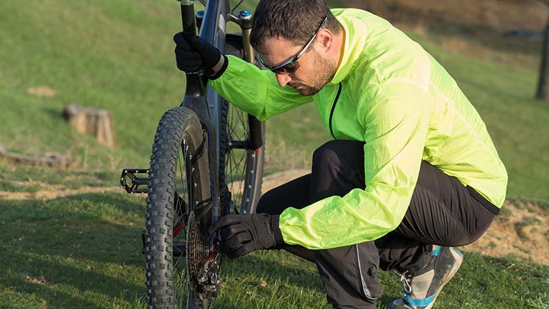 En mann står på huk ved en sykkel og sjekker dekkene.
