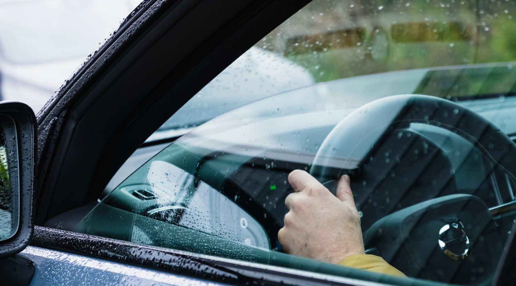 Nærbilde av førerdøren på en bil, man ser en hånd på rattet på innsiden gjennom et vindu på gløtt.