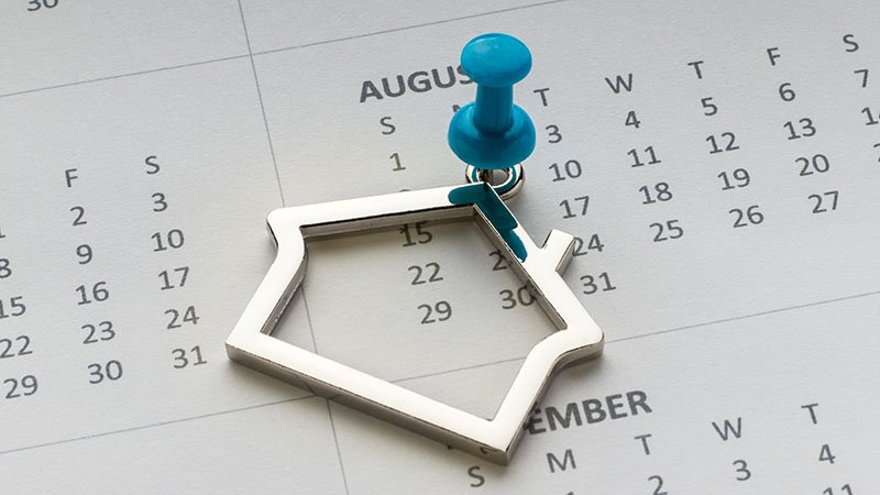 Metallnøkkelring formet som et hus festet med en blå tegnestift på en kalender.