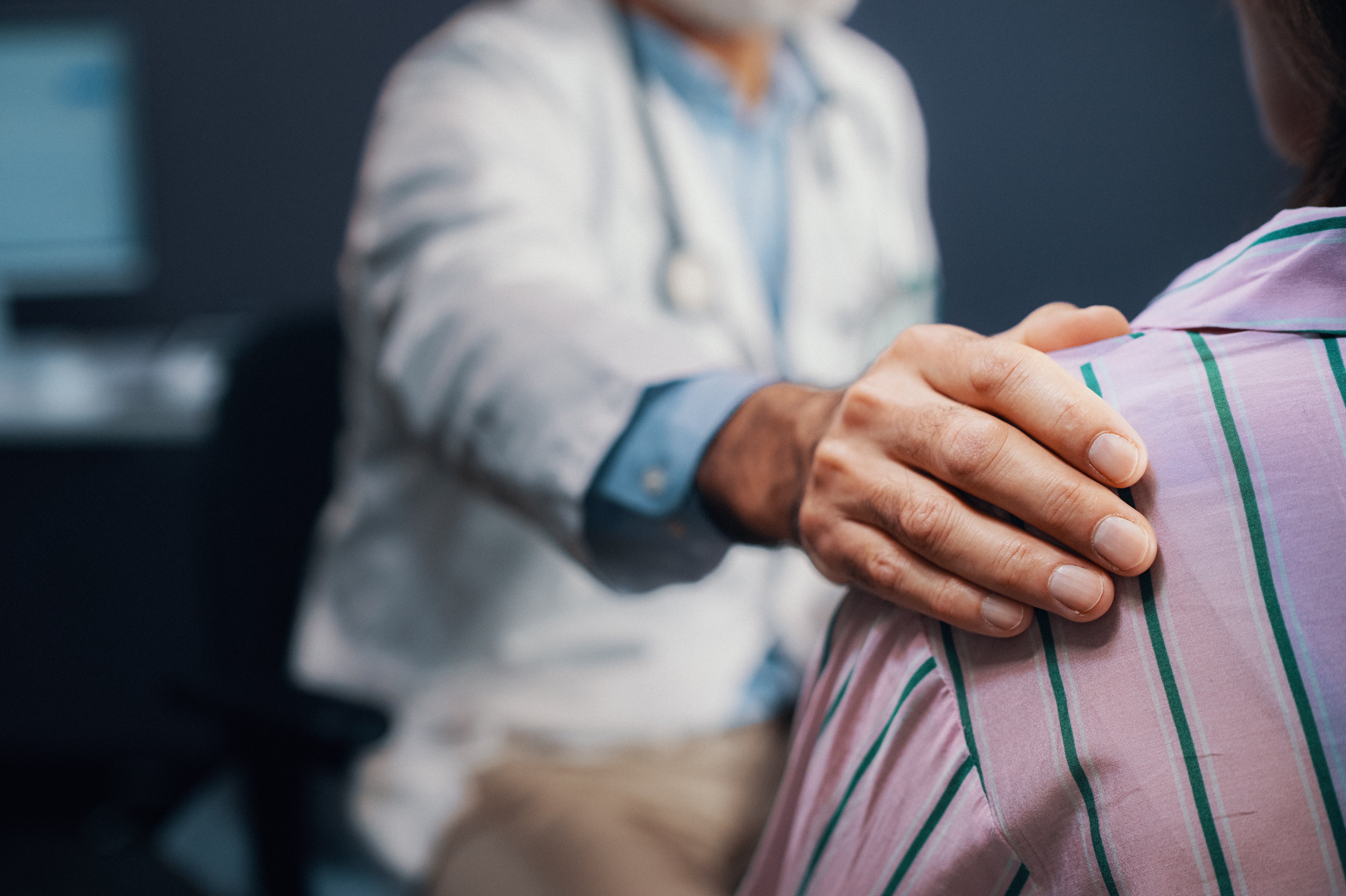 En lege har hånden på skulderen til en pasient under en konsultasjon.