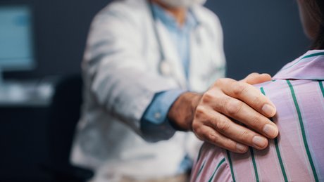 En lege har hånden på skulderen til en pasient under en konsultasjon.