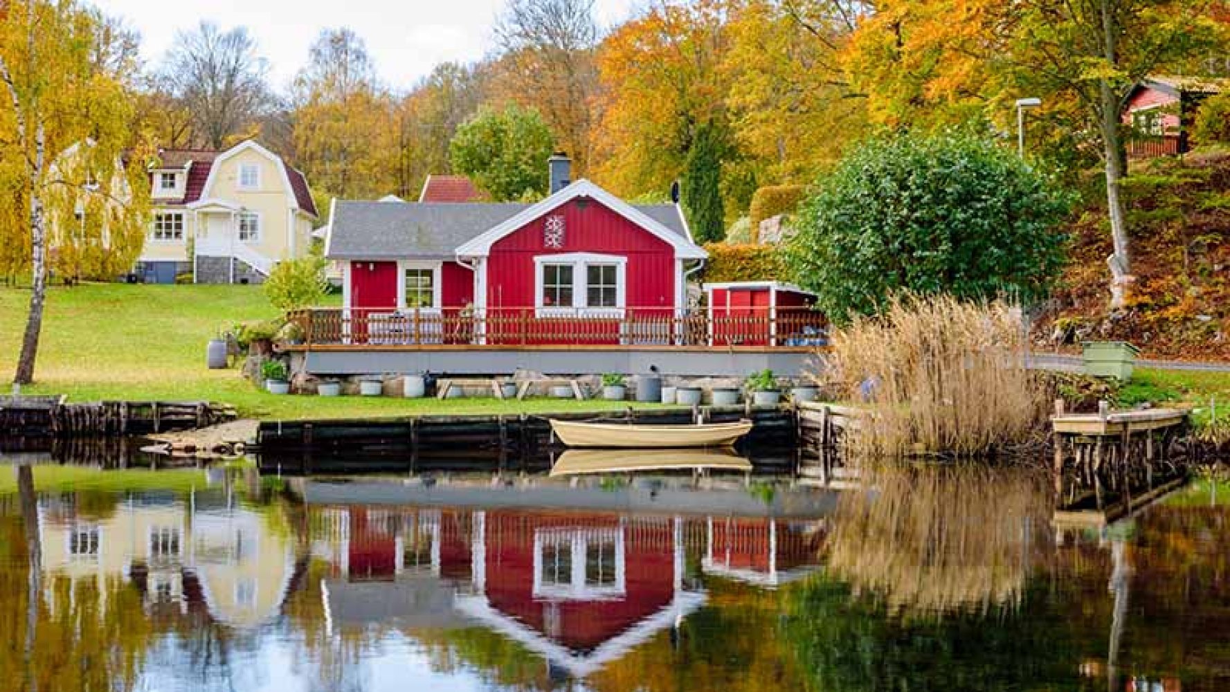 Rød hytte ved innsjø med høstfargede trær i bakgrunnen