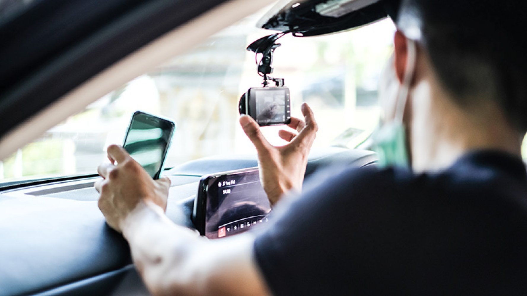 Person monterer dashbordkamera i bil og holder en mobiltelefon